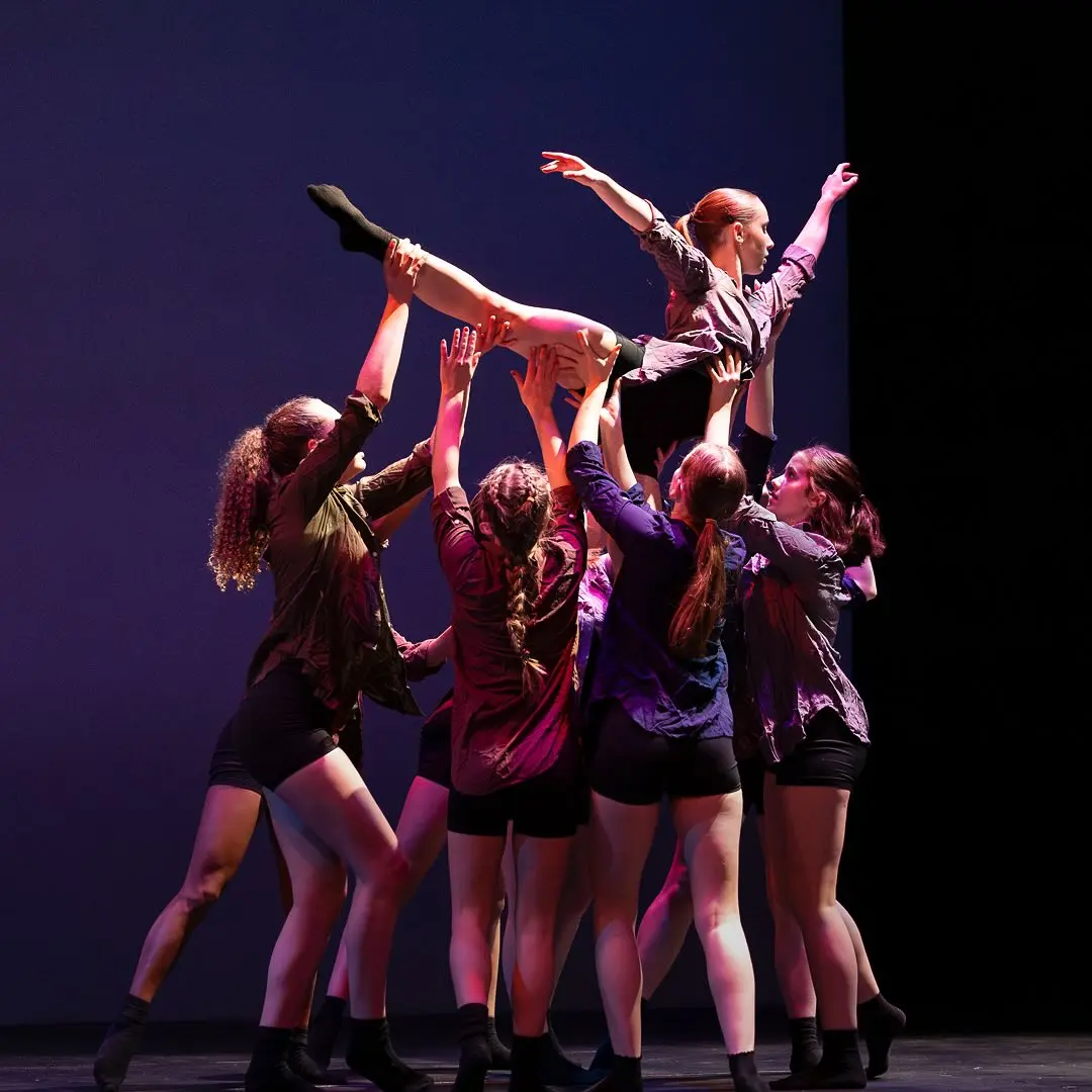 A group of dancers performs a lift on stage.