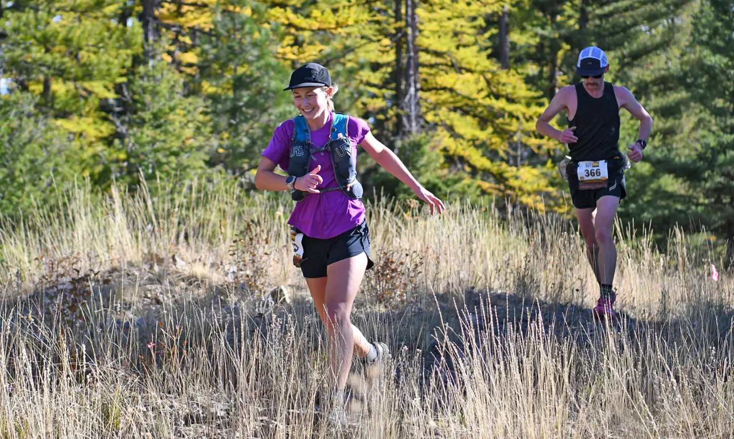 Two runners participate in a trail race through a wooded area.