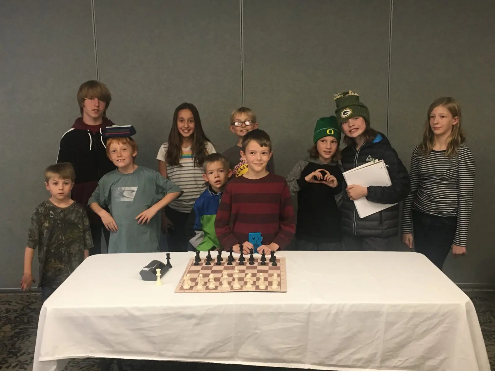 A group of children standing behind a table with a chessboard.
