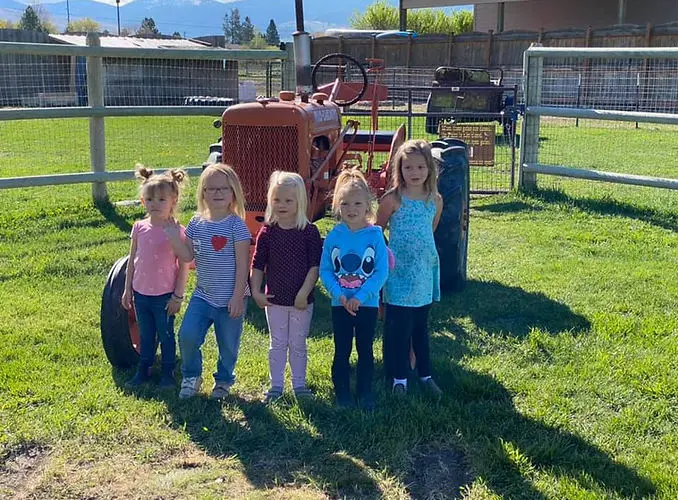 Five young children pose for a photo in front of a tractor.