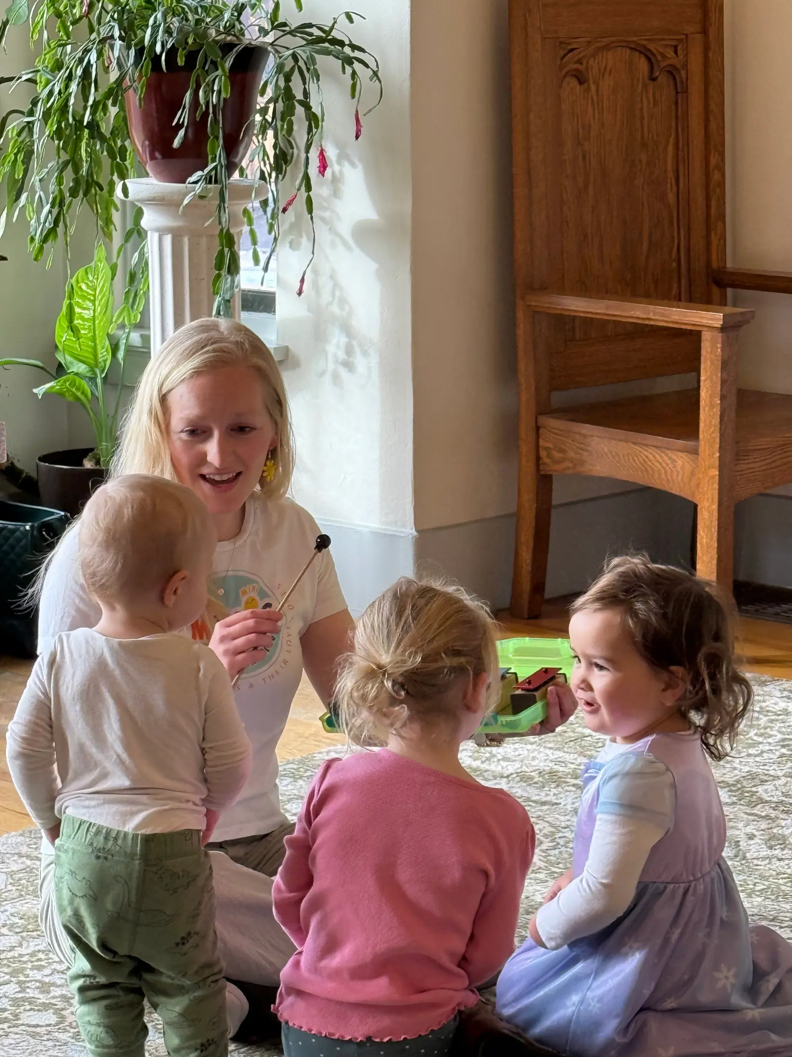 A teacher leads a small group of children in a music activity while sitting on a rug.