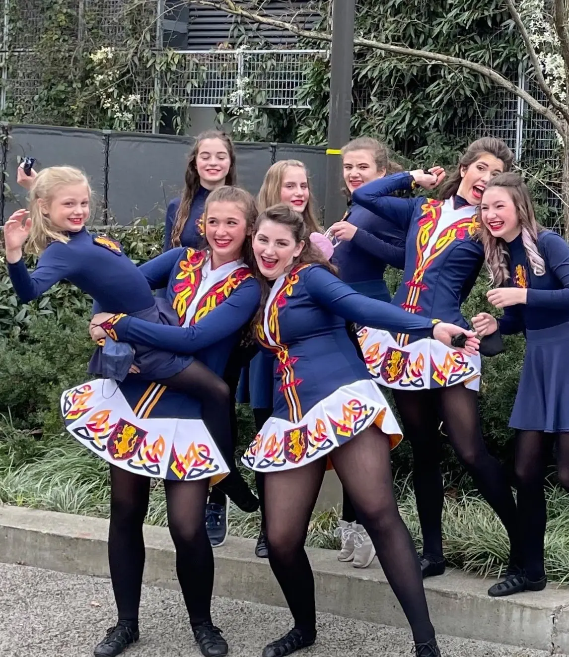 A group of Irish dancers in matching costumes pose outdoors.