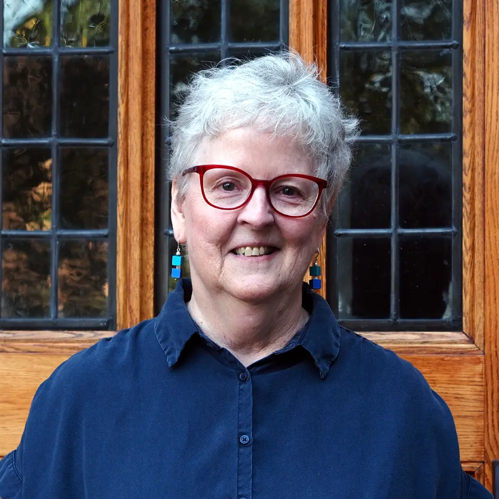 A woman with gray hair and red-framed glasses poses for a portrait.