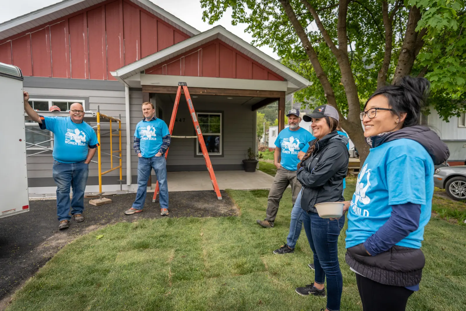 A group of adults in matching blue shirts gather at a construction site for a home project.