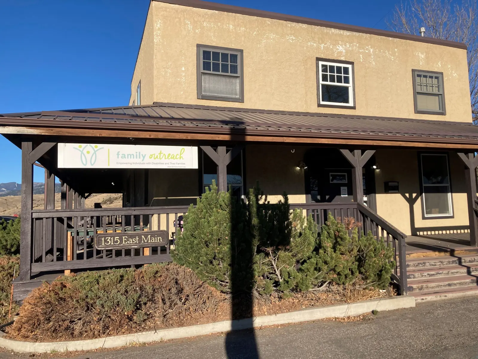 A tan building with a covered porch features a sign for family outreach and a street address.
