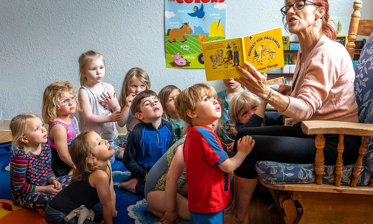 An instructor reads a book to a group of young children sitting on a rug.