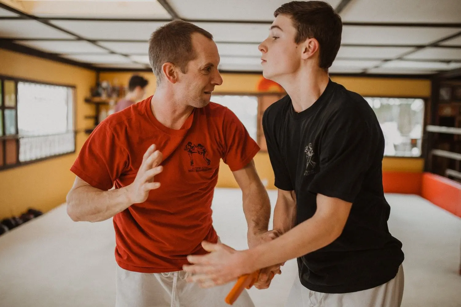 An instructor and a student engage in martial arts practice in a training studio.