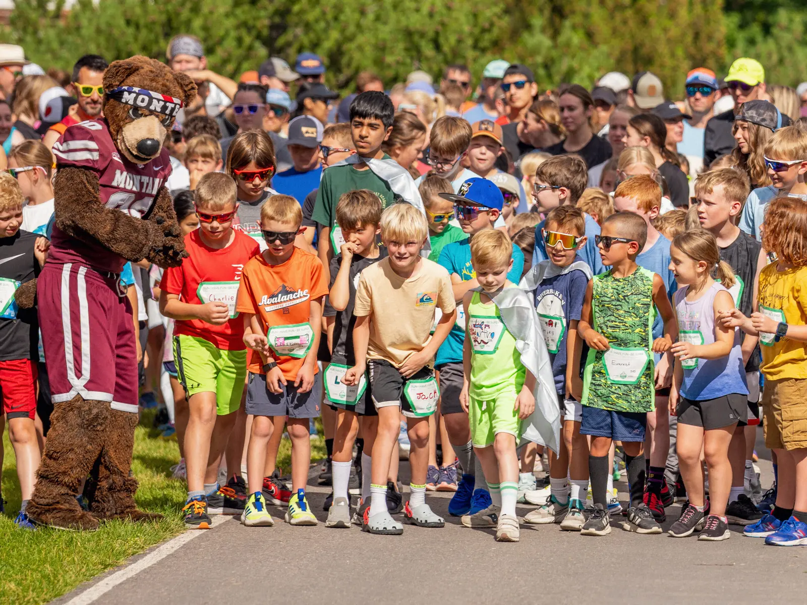 A mascot interacts with a group of children at the starting line of a race.