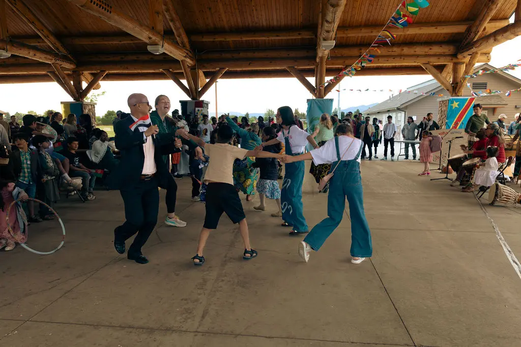 People are dancing together at an outdoor community event held under a pavilion.