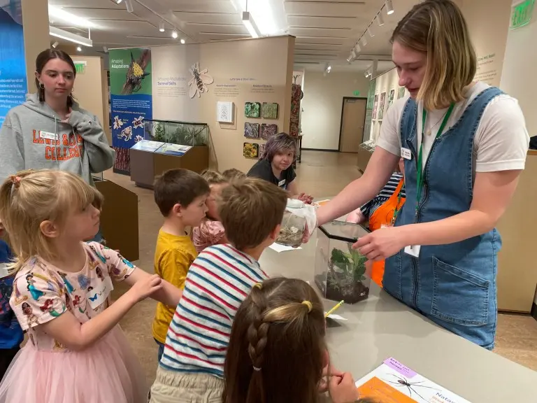 An instructor shows a container with a specimen to a group of children at a nature center.