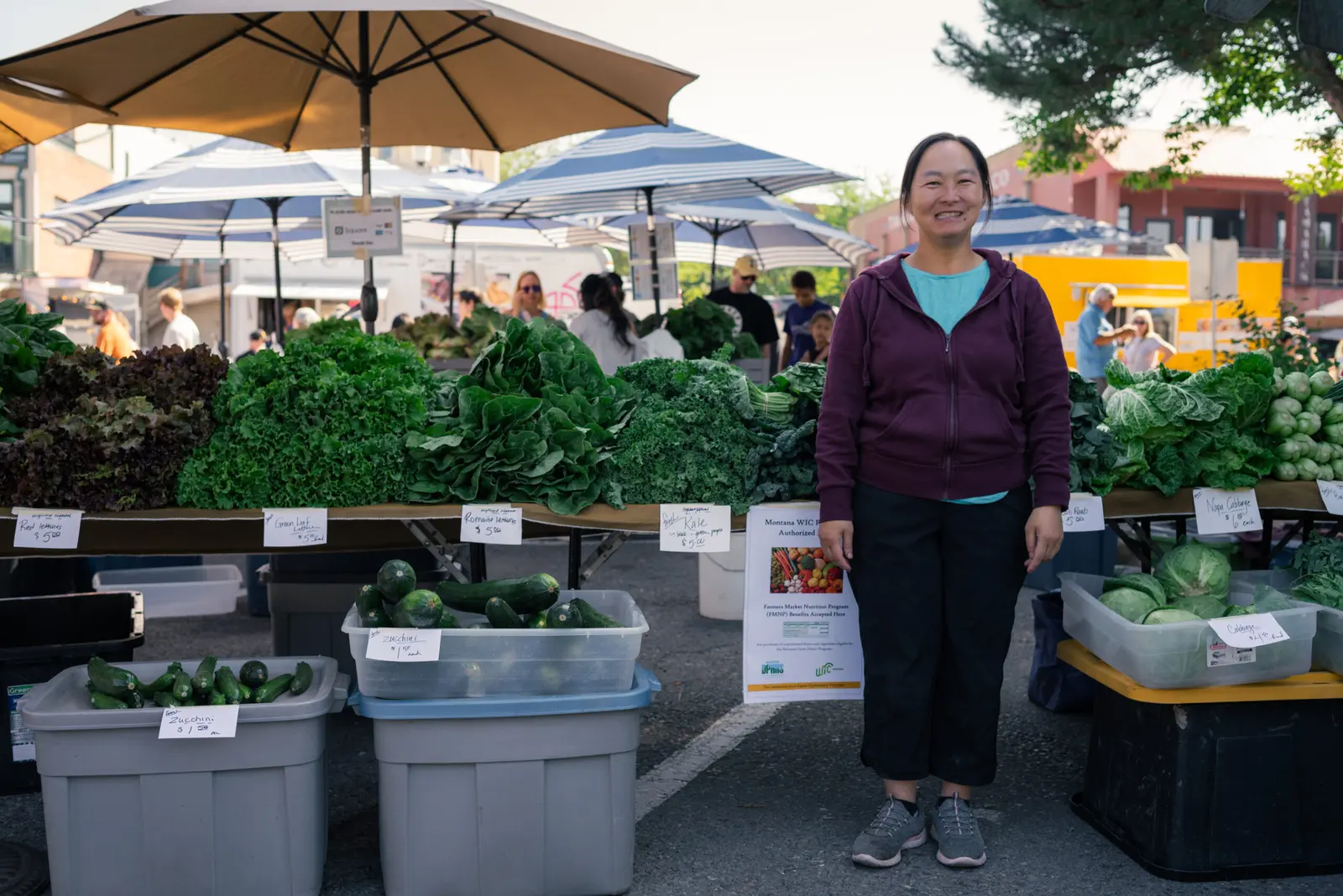 A woman stands in front of a market stall selling various fresh produce.
