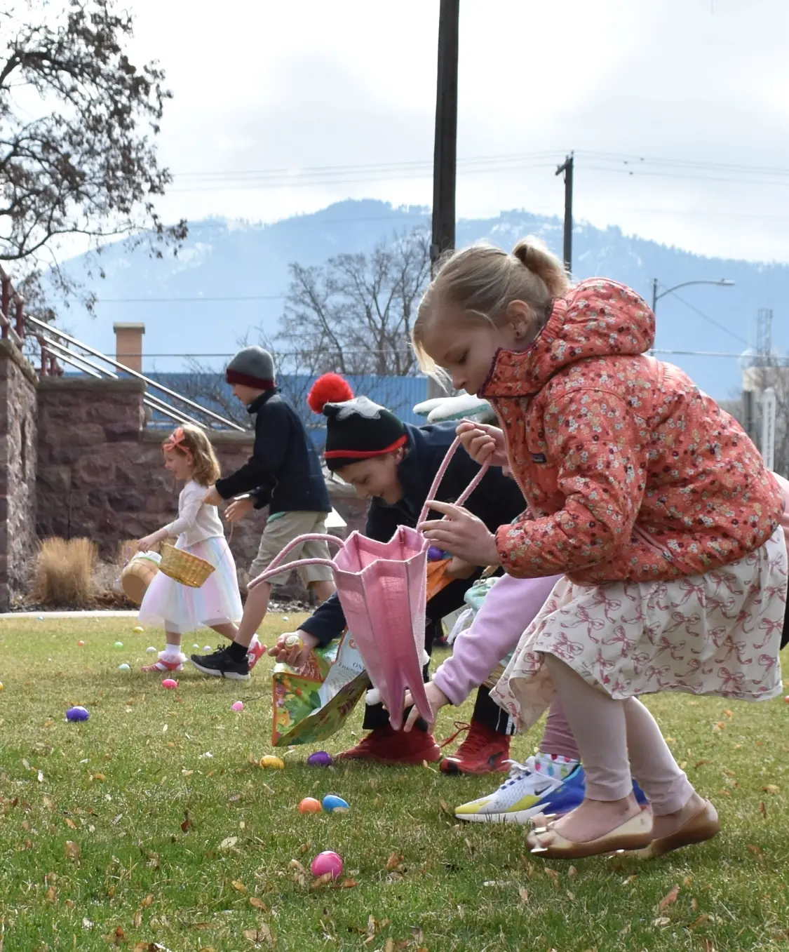 Several children participate in an outdoor Easter egg hunt on a lawn.