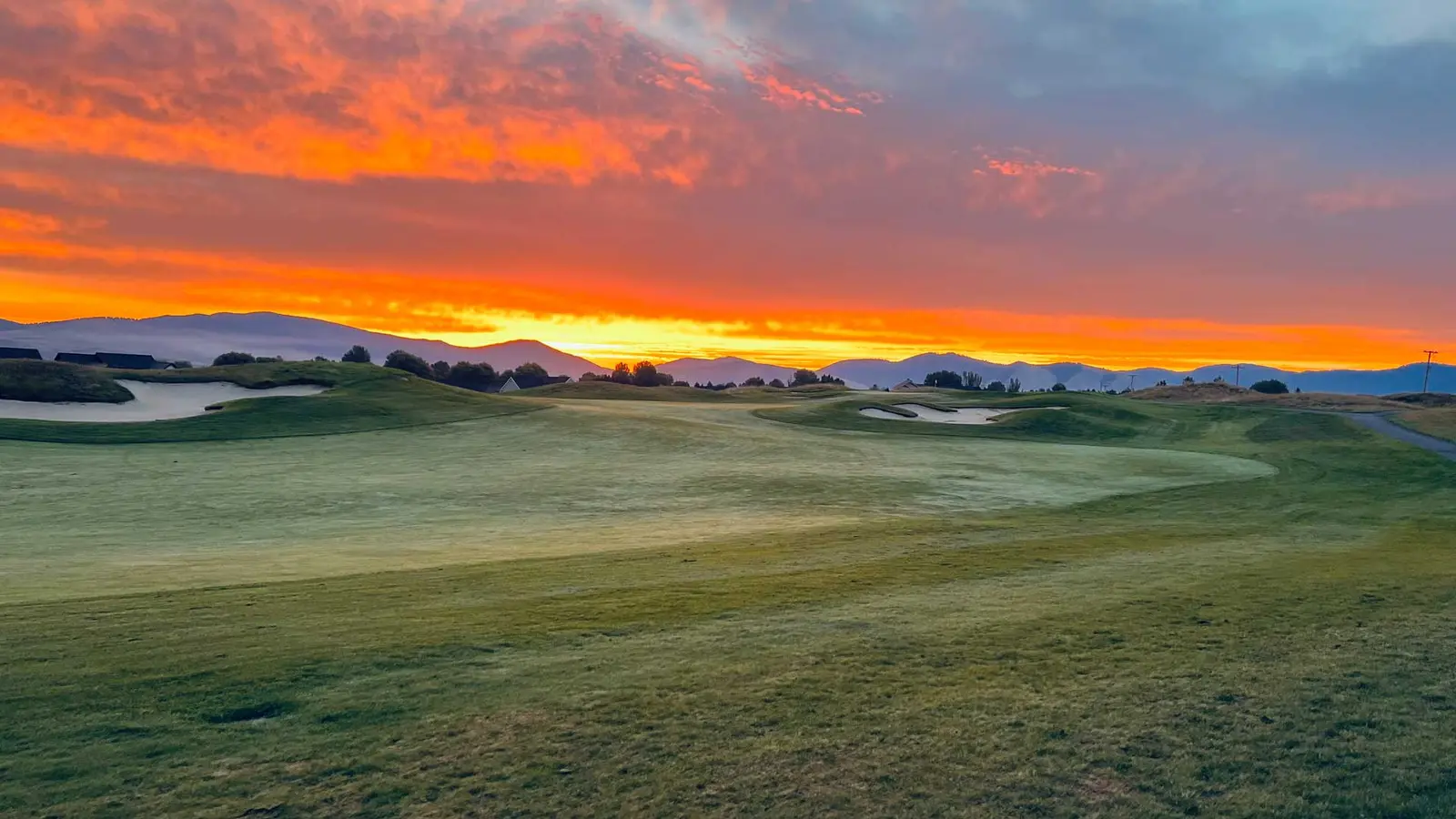 A vibrant sunrise illuminates a golf course with mountains in the background.