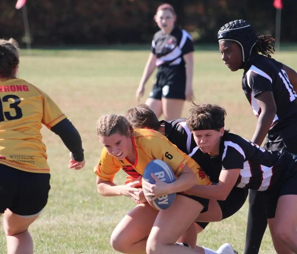 A group of young women participate in a competitive rugby match on a field.