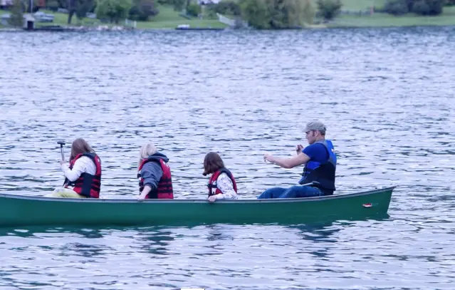 A group of people wearing life jackets paddle a canoe on a lake.