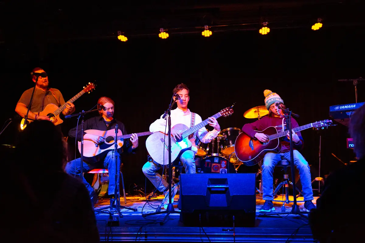 A band performs on stage with acoustic guitars and microphones.