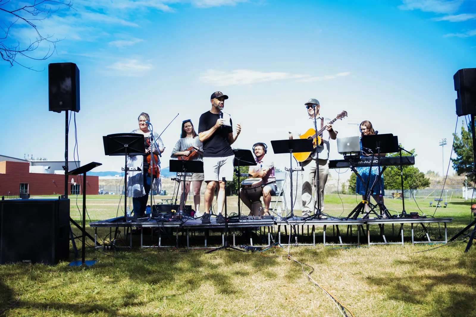 A musical group performs on an outdoor stage in a grassy area.