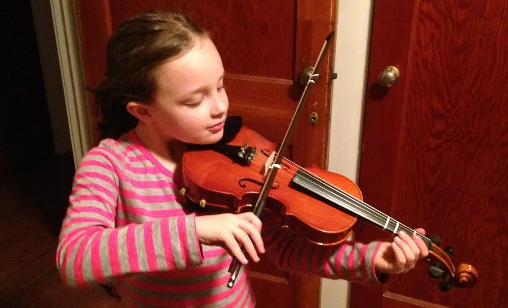 A child plays a violin in front of a wooden door.