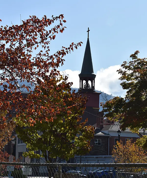 A steeple rises above buildings, framed by trees in autumn foliage.