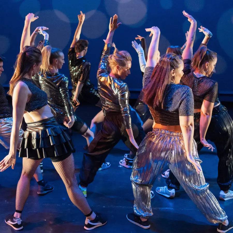 A group of dancers in metallic and shiny outfits perform on stage.