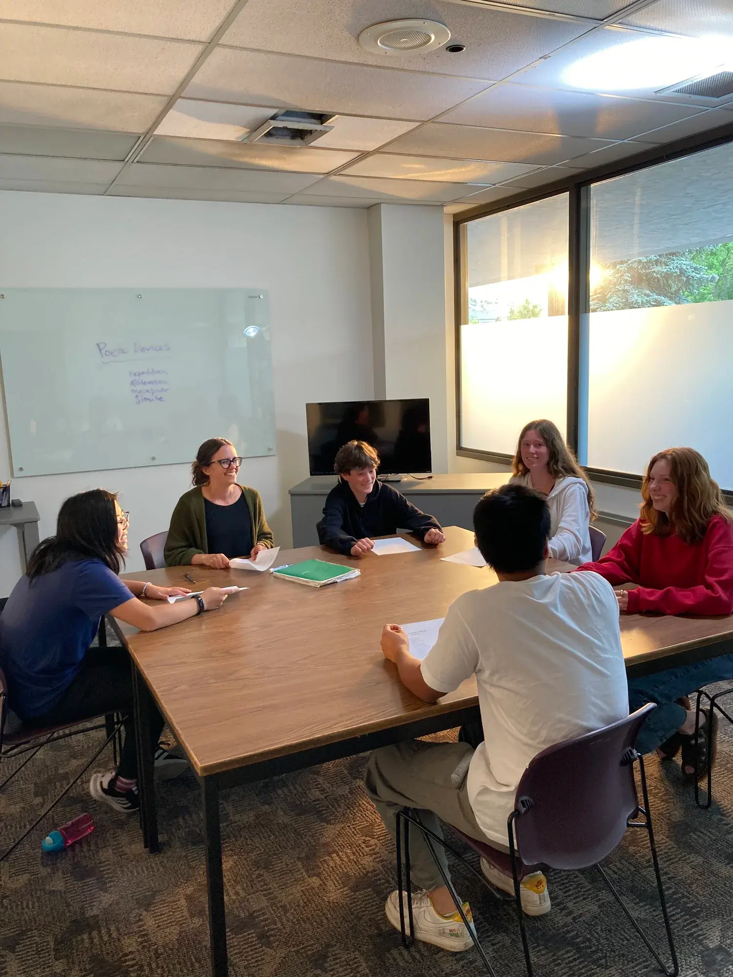 An instructor leads a group of students in a discussion around a table in a classroom.