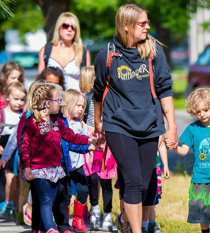An instructor leads a group of children walking outdoors.