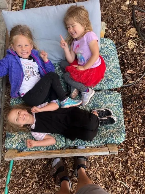 Three young children sit and lie on cushioned outdoor chairs.