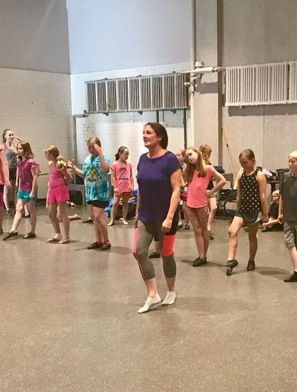 An instructor leads a group of children in a dance practice session.