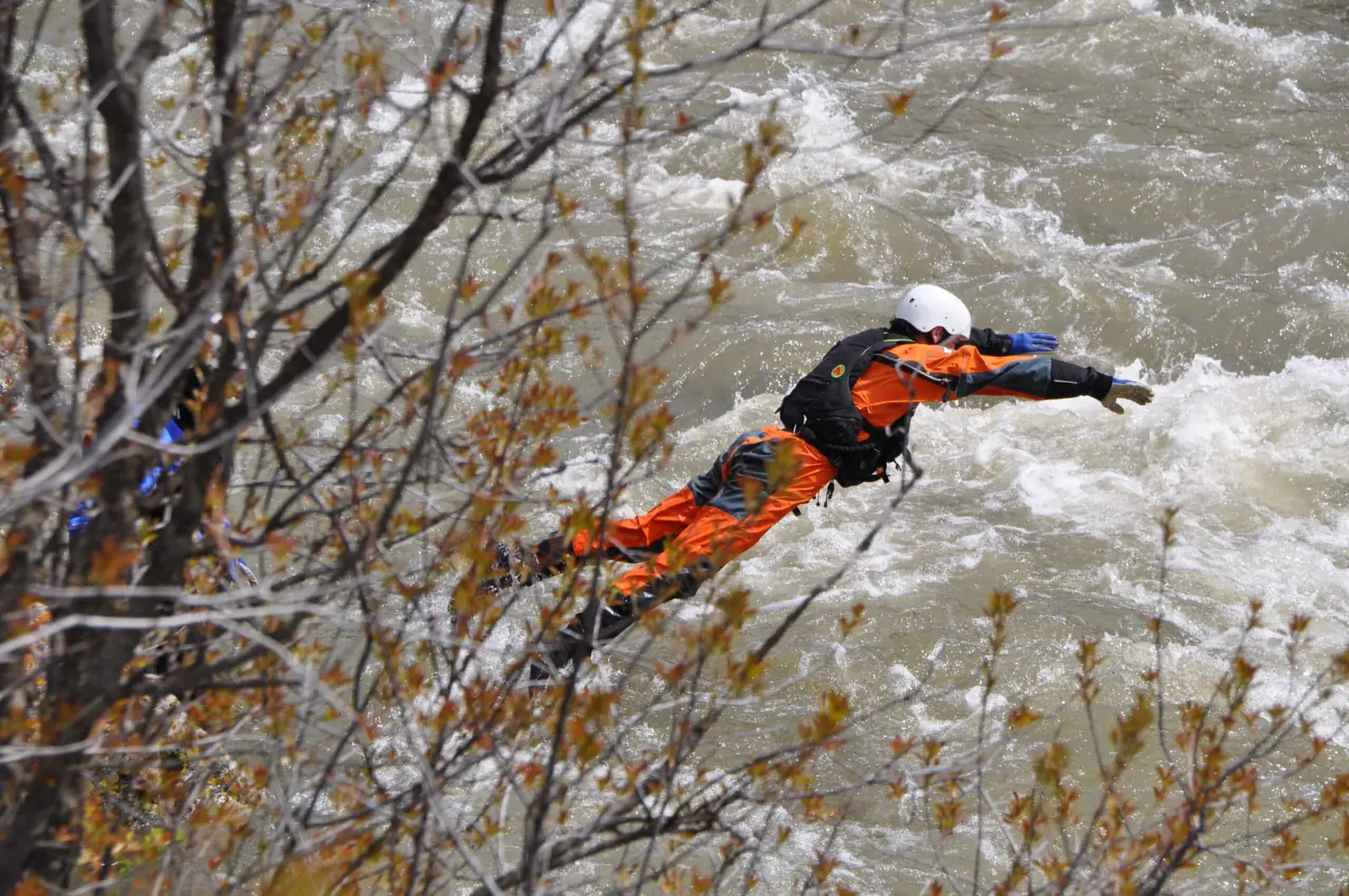A person in professional rescue gear leaps into the rushing water of a river.