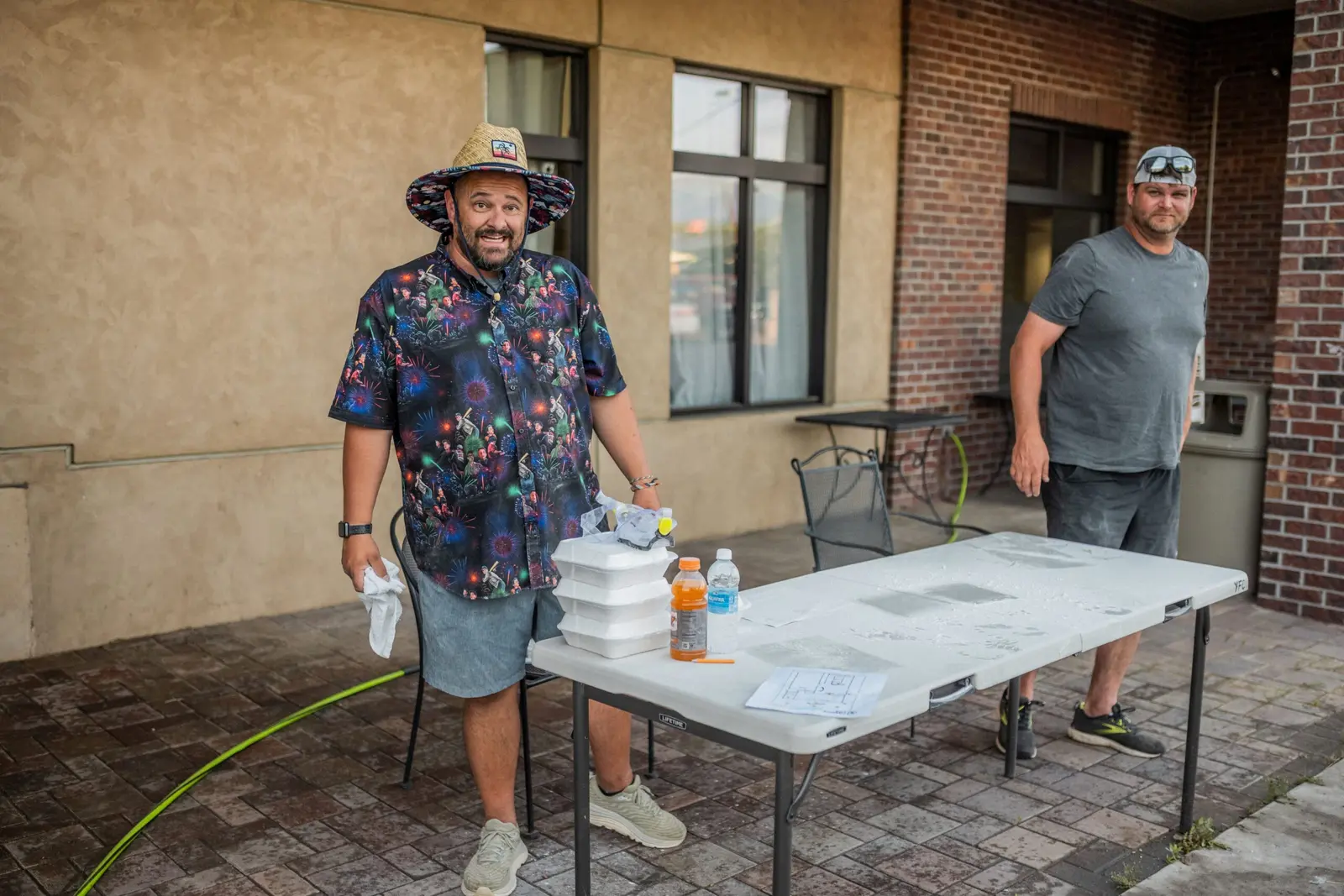 Two men stand outdoors near a folding table with supplies.