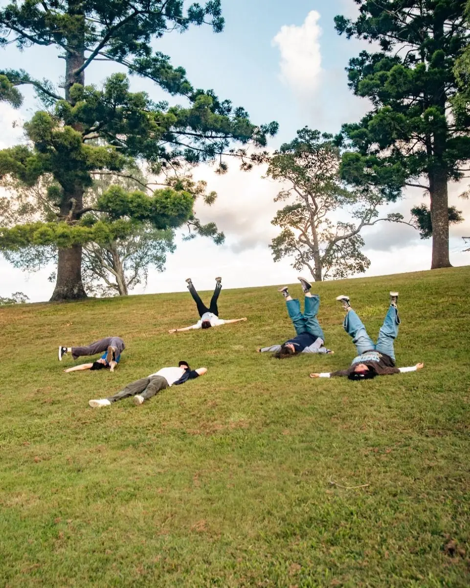 A group of young people lie on a grassy hill with their legs in the air.