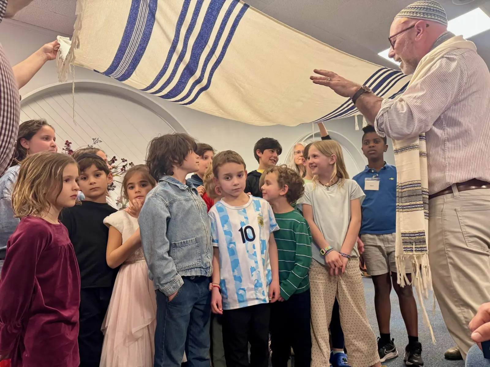 Children standing hnder a canopy being blessed by a rabbi.