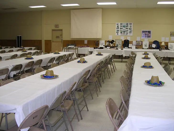 An empty event hall features rows of tables decorated with hats.