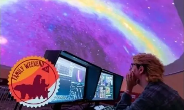 A person looks at computer screens in a dark room under a colorful projection on the ceiling.