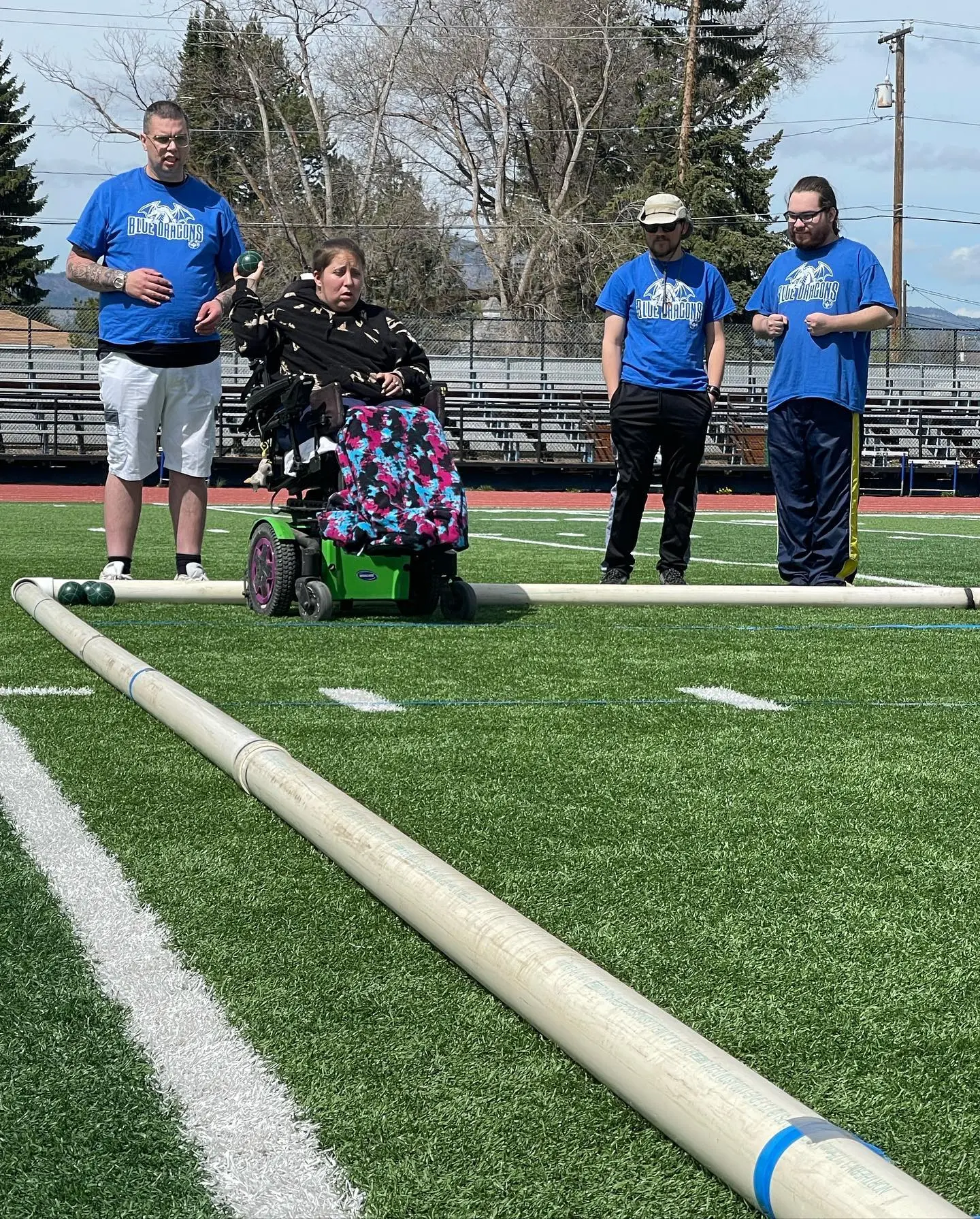 A group of adults in Blue Dragons shirts participate in a bocce ball game on a field.