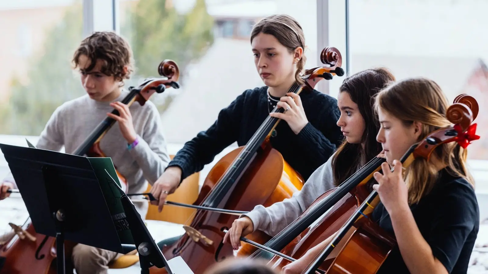 A group of young people play cellos together in an orchestra setting.