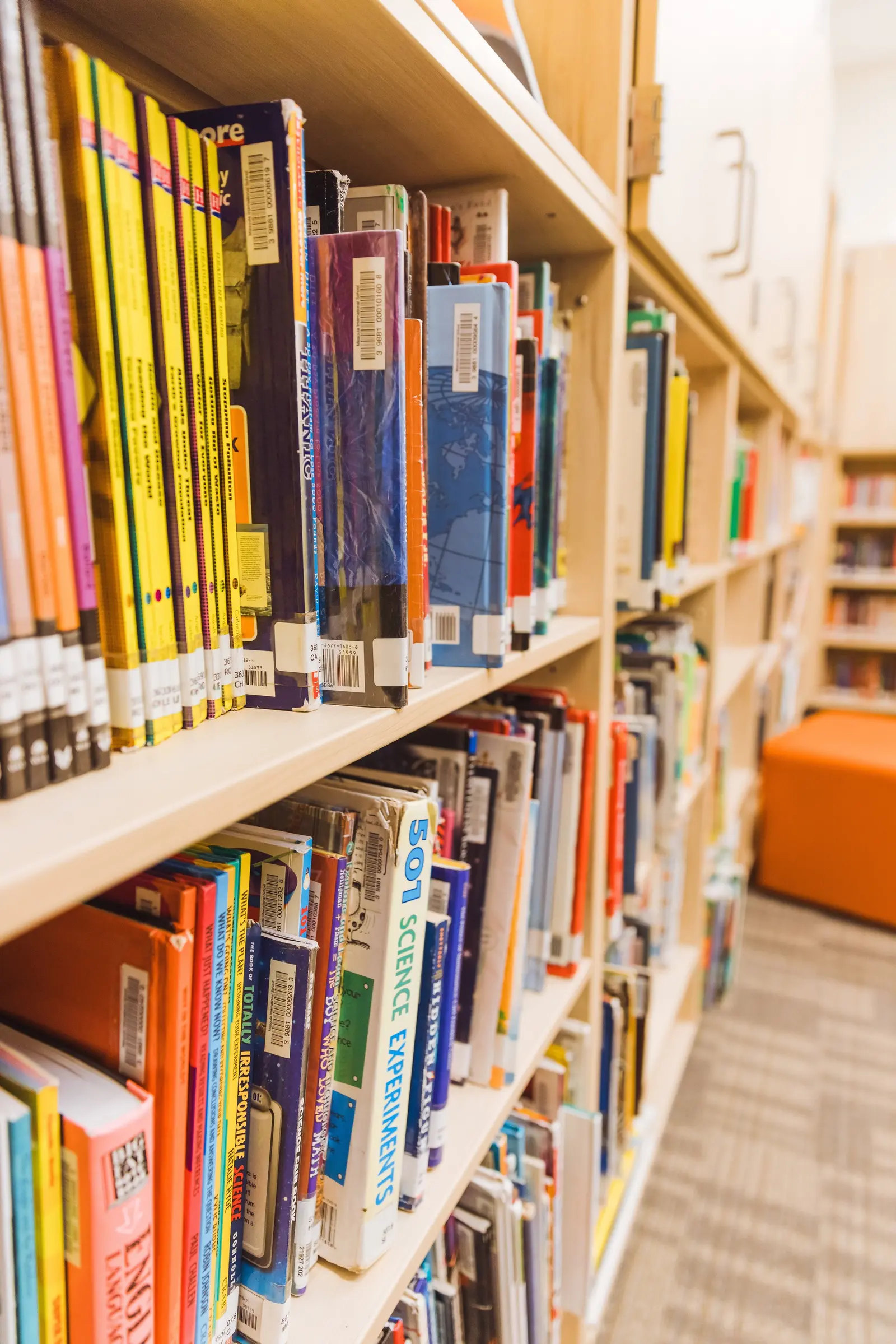 Rows of colorful books are lined up on wooden library shelves.