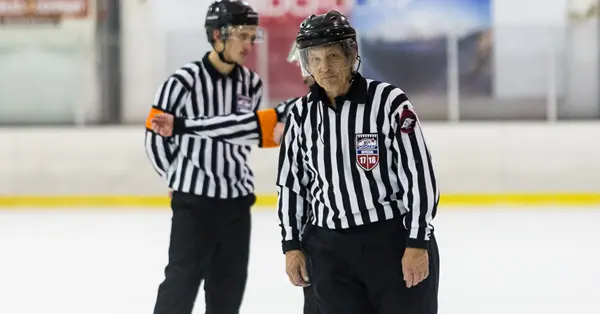 Two ice hockey referees in striped uniforms stand on the ice rink.