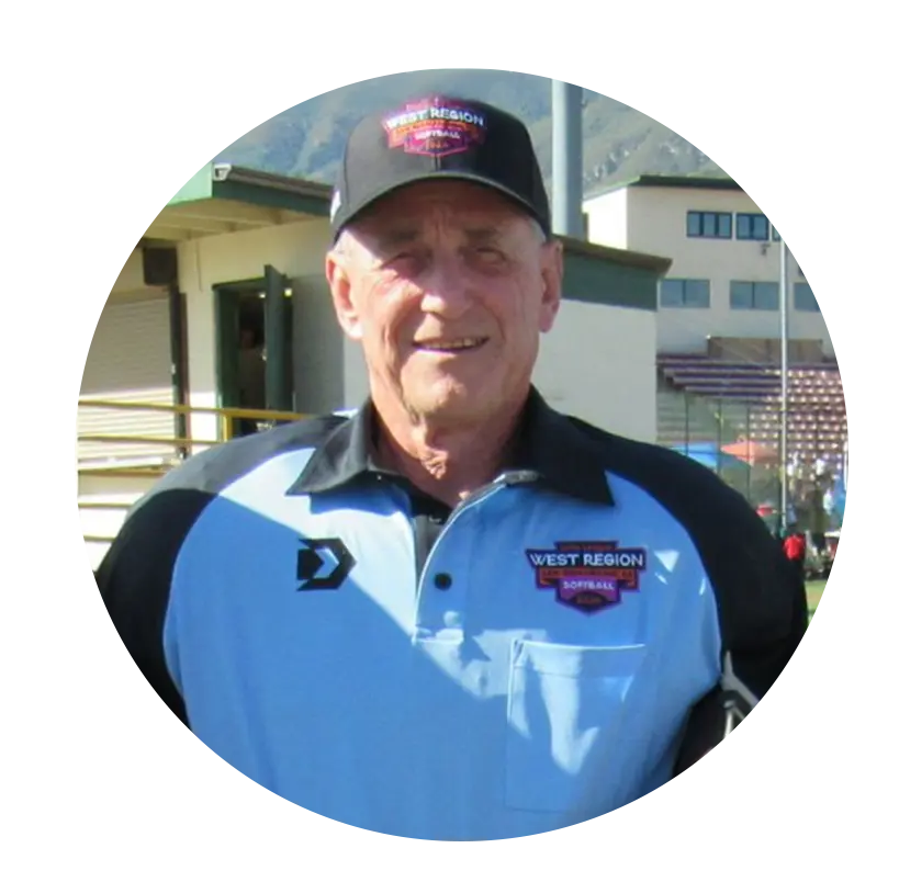An adult man in a softball official uniform poses for a portrait on a field.