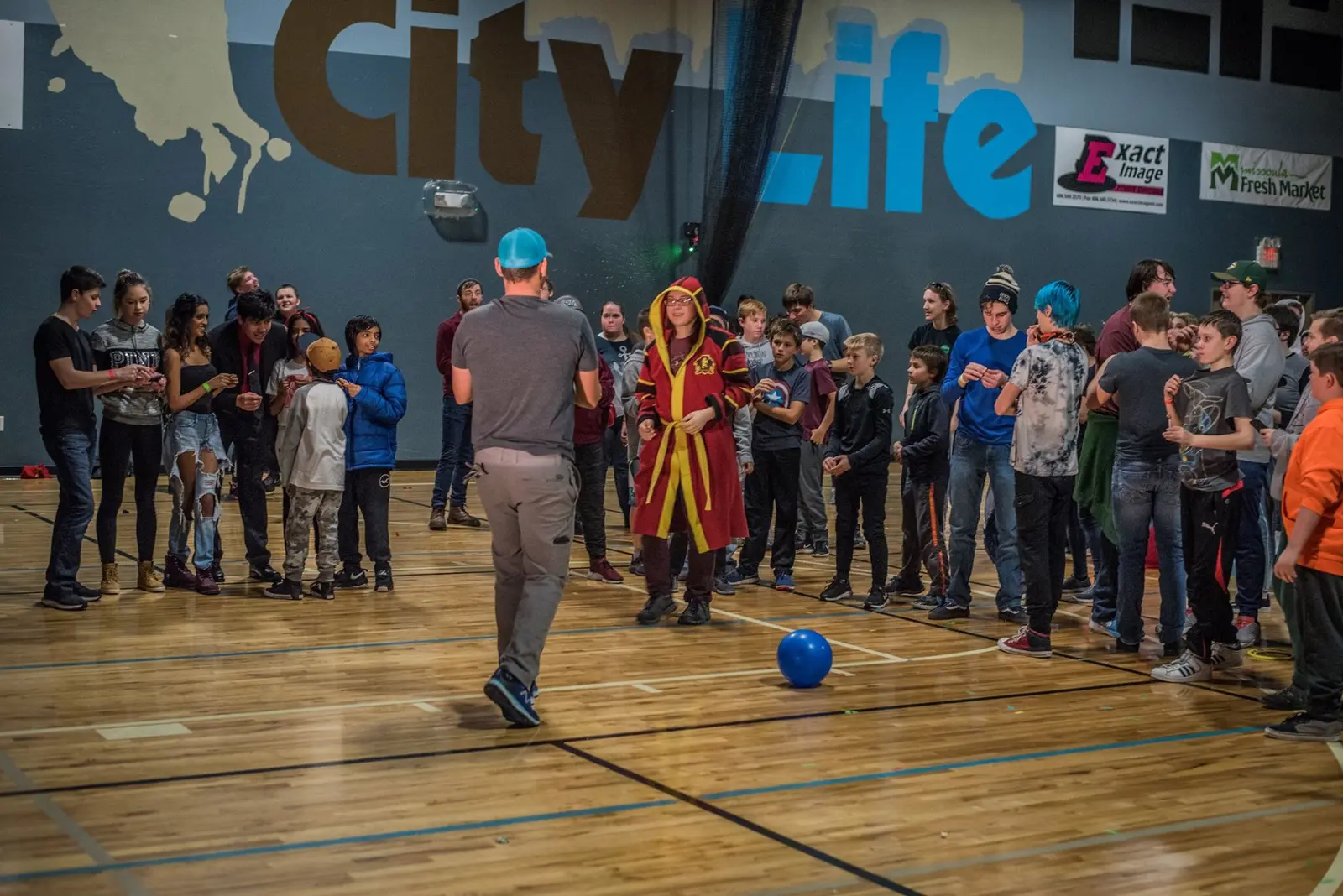 A group of young people and an instructor gather in a gymnasium during an activity.