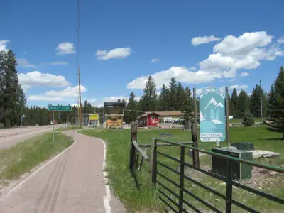 Photo from missoulacounty.gov A paved path leads past a welcome sign and trees on a sunny day.