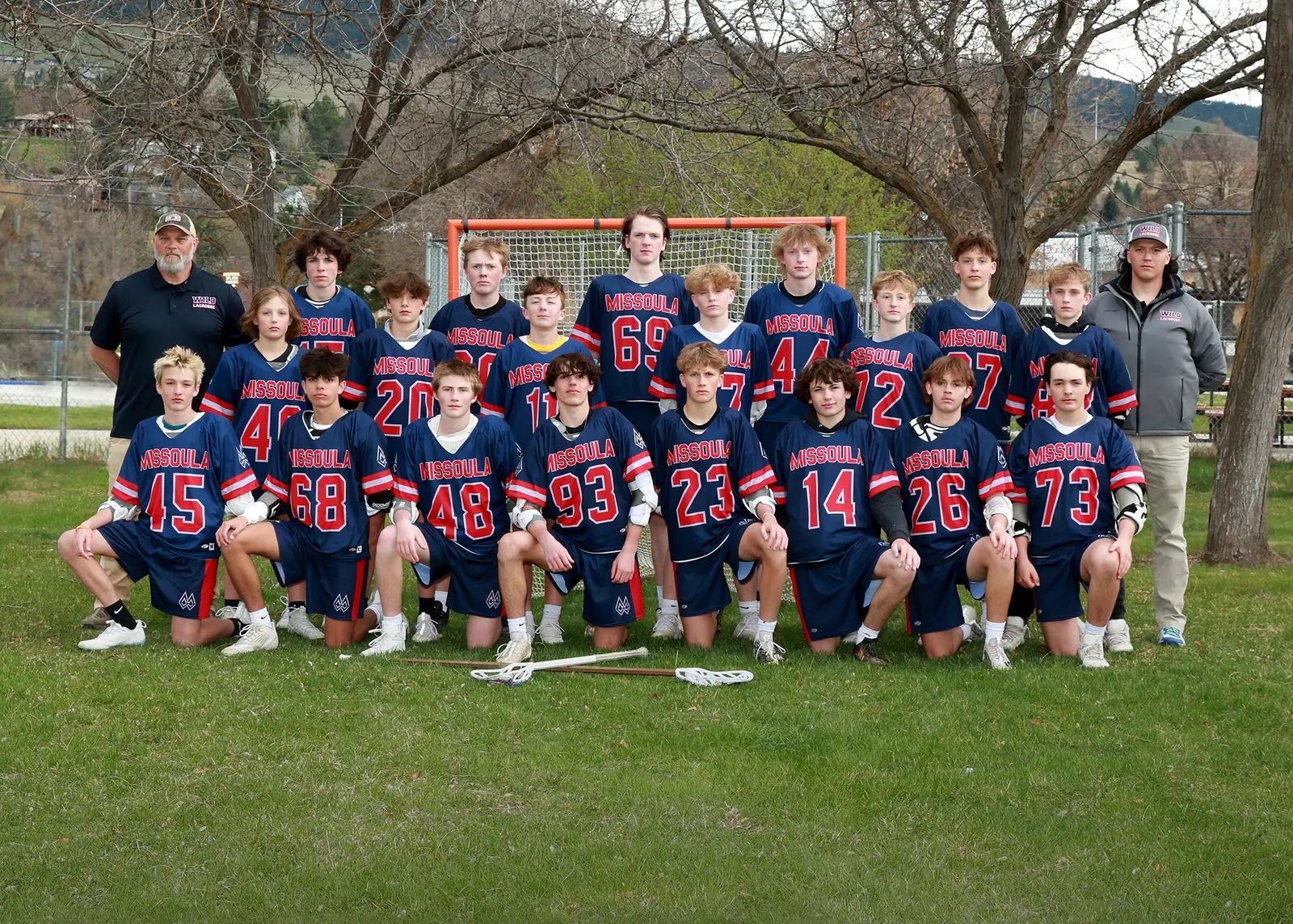 A lacrosse team poses for a group portrait with their coaches on a field.