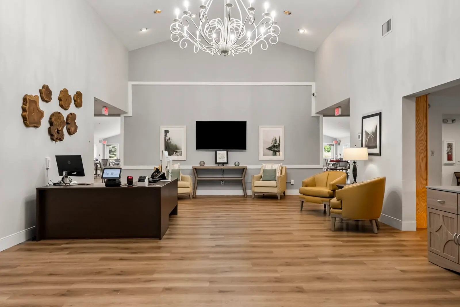 A bright, modern lobby or reception area features wood flooring, comfortable seating, a front desk, and a large chandelier.
