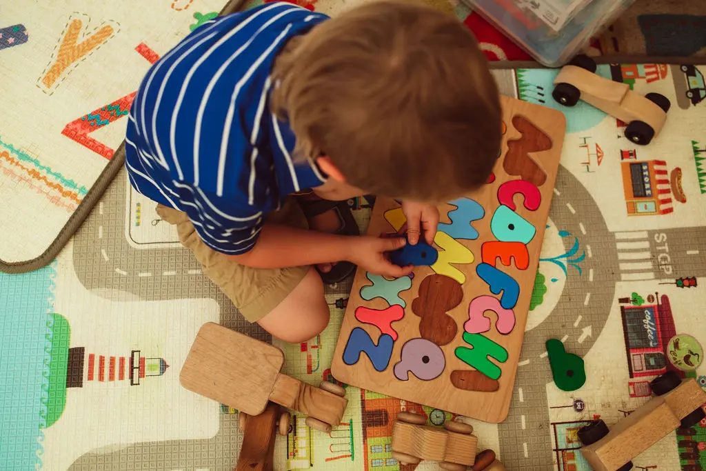 A child is sitting on a play mat while playing with an alphabet puzzle.