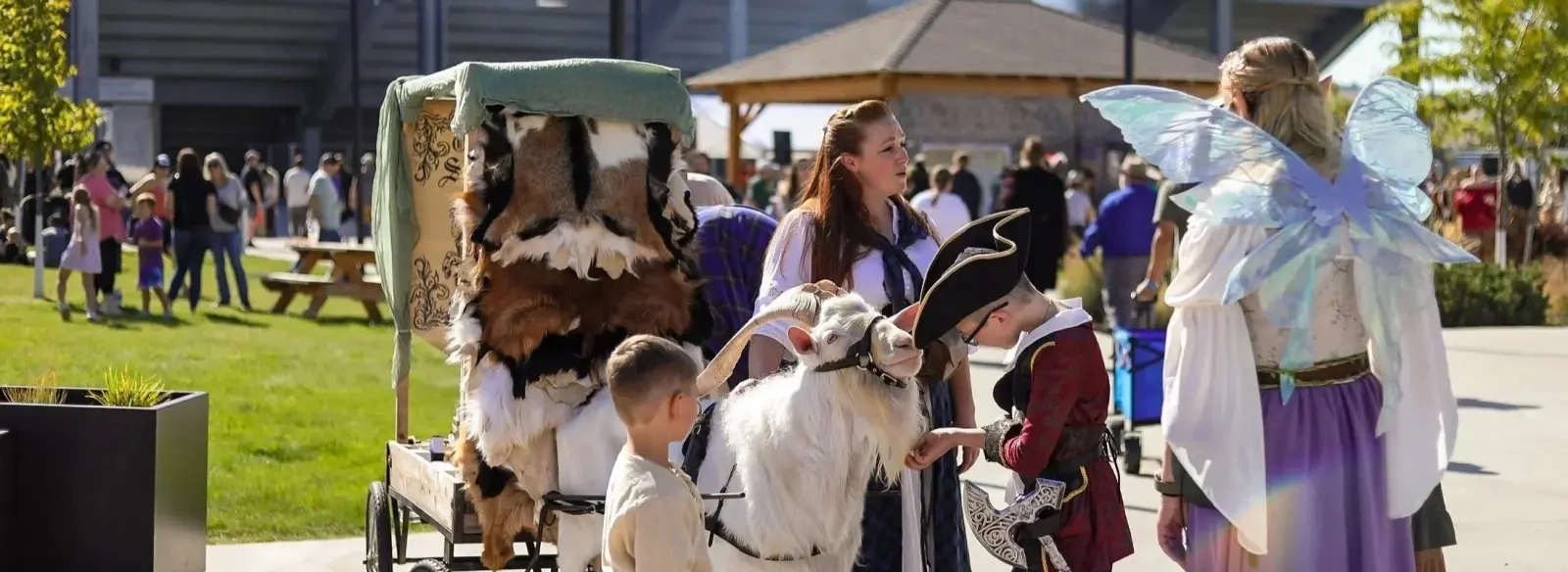 People dressed in costumes interact with a goat at an outdoor event.