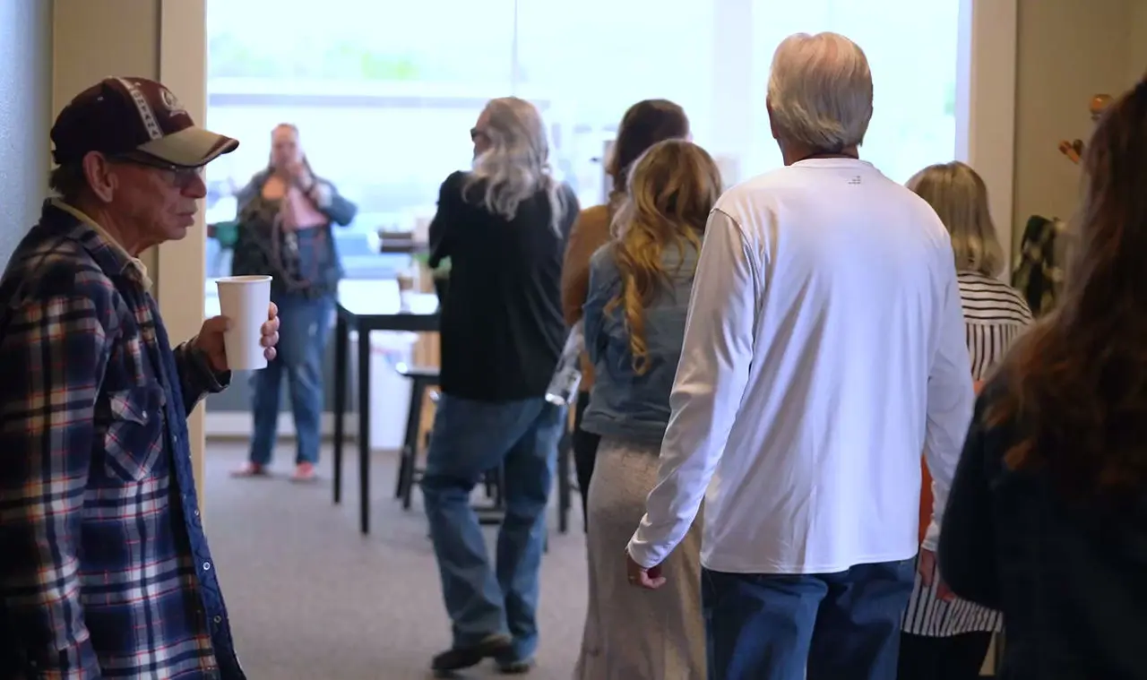 A group of adults stands in an indoor space, with one person in the foreground holding a paper cup.