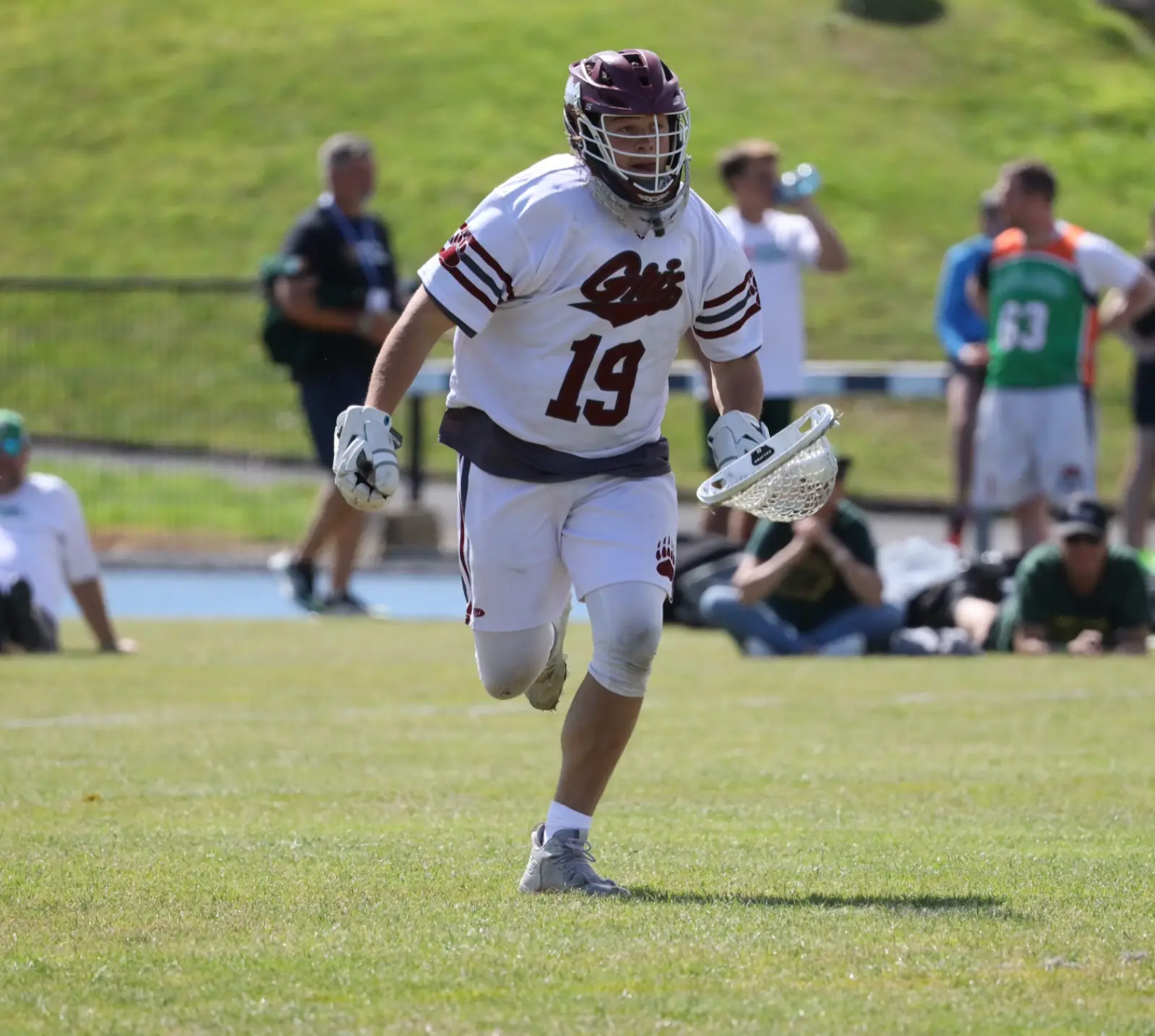 A lacrosse player in a white uniform runs across a field during a game.