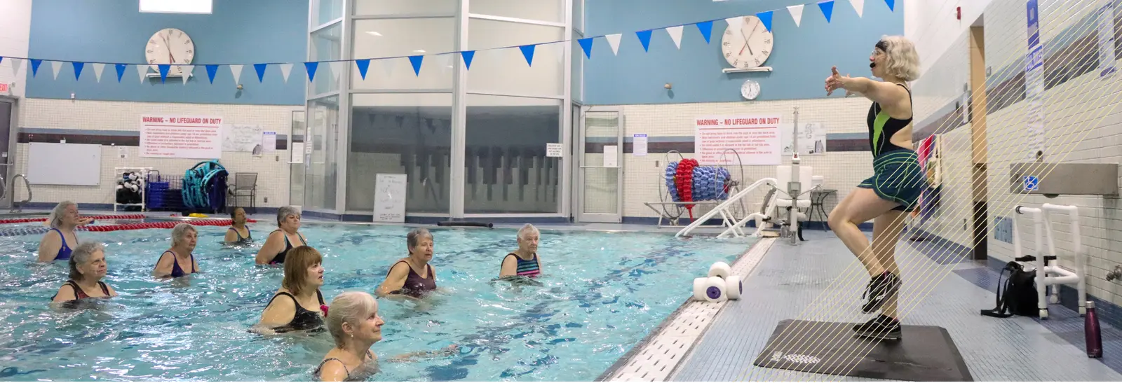 A woman leads a water aerobics class for a group of adults in an indoor pool.