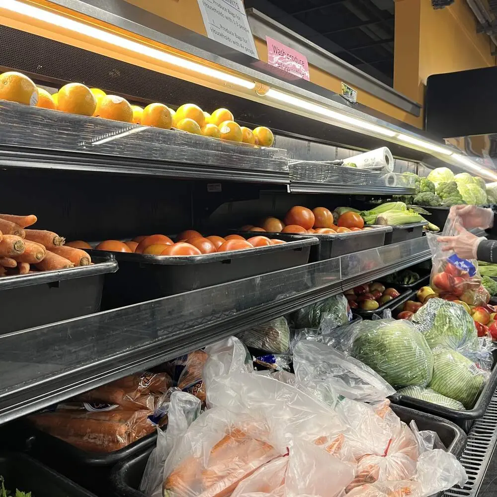 A person's hand reaches for produce at a grocery store shelf.
