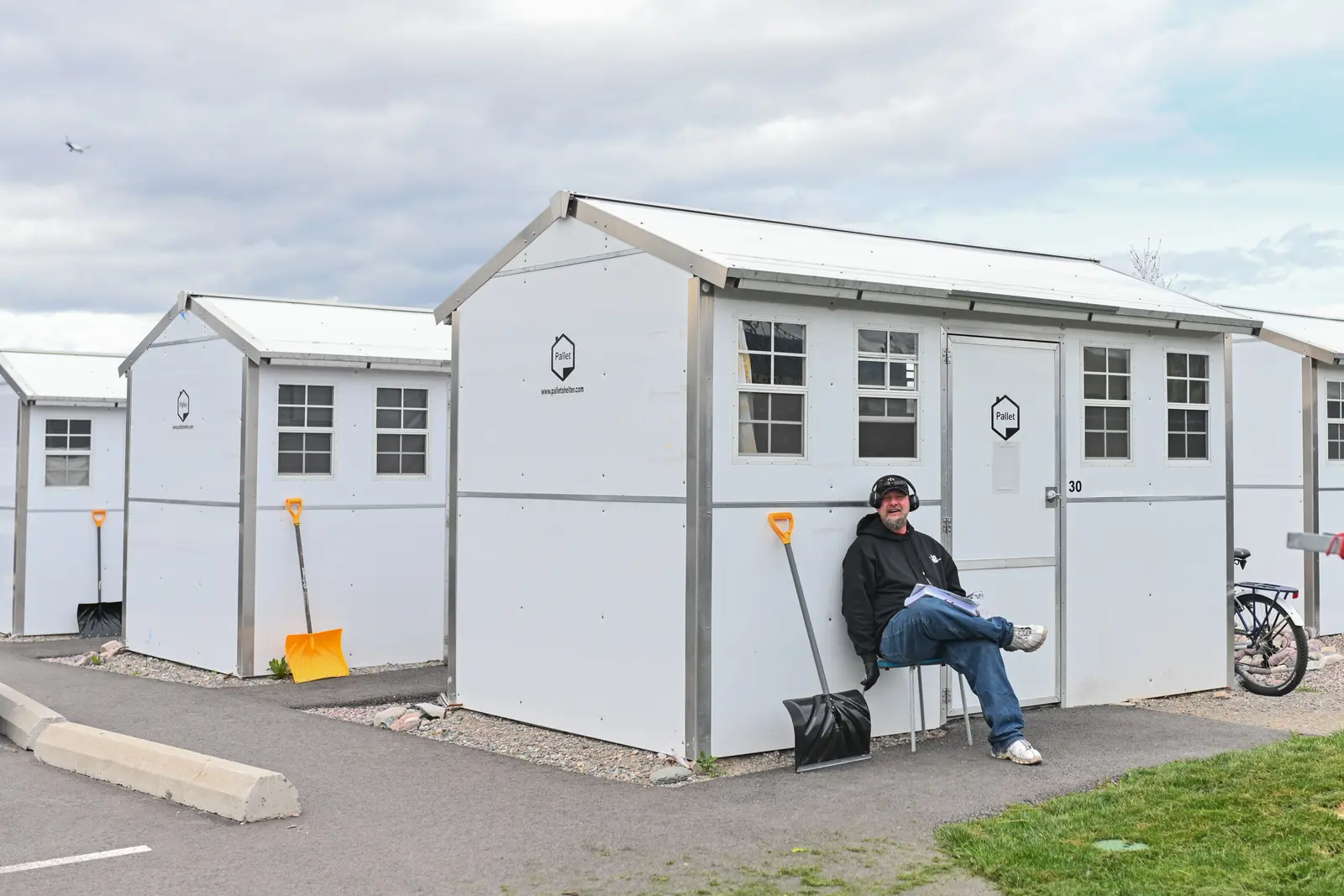 A man sits on a chair in front of a small white shelter structure.